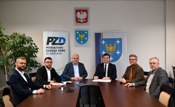 Na sali konferencyjnej przy stole siedzi 6 osób uczestniczących w podpisaniu umowy.